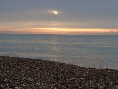 Denizin üzerinde gün doğarken, küçük bir yelkenli görünür.