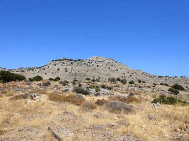 Kuru arazide tepeler, kuru otlar ve kayalar.