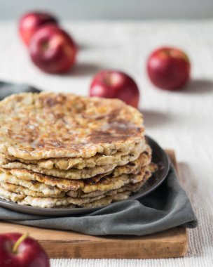 El yapımı tam buğday unlu tortilla yığını keten masa örtüsü üzerinde kırmızı elmalar arka planda, seçici bir odaklanma