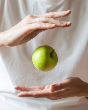 Tüm yeşil elma, beyaz arka planda, seçici bir odak noktasında, ellerinin üzerinde havaya yükselir. Sağlıklı yeme kavramı