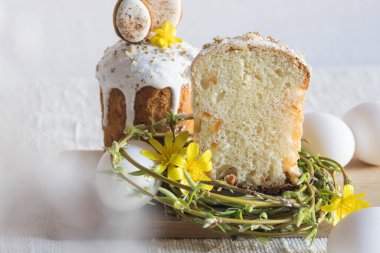 Paskalya kurabiyeleriyle süslenmiş geleneksel paskalya pastası, yuva şeklinde söğüt dalları, sarı çiçekler, keten masa örtüsünün üzerinde beyaz yumurtalar. Yan görüş, seçici odaklanma. Paskalya ziyafeti, tatil sembolü