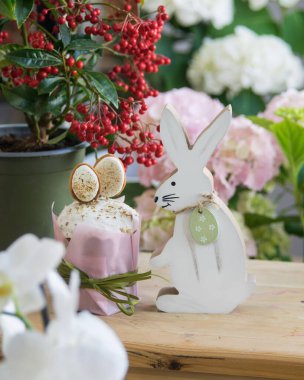 Paskalya süsleri. Paskalya oyuncağı tahta tavşan, renkli yumurta, Paskalya pastası ve masada çiçekler..