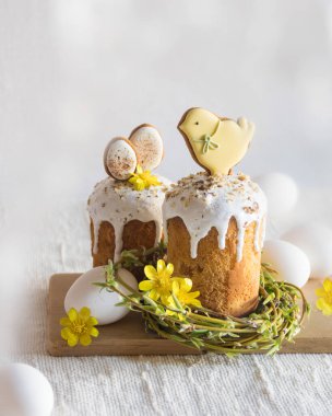 Paskalya kurabiyeleriyle süslenmiş geleneksel paskalya pastası, yuva şeklinde söğüt dalları, sarı çiçekler, keten masa örtüsünün üzerinde beyaz yumurtalar. Yan görüş, seçici odaklanma. Paskalya ziyafeti, tatil sembolü