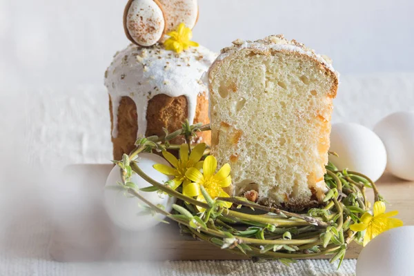 Paskalya kurabiyeleriyle süslenmiş geleneksel paskalya pastası, yuva şeklinde söğüt dalları, sarı çiçekler, keten masa örtüsünün üzerinde beyaz yumurtalar. Yan görüş, seçici odaklanma. Paskalya ziyafeti, tatil sembolü