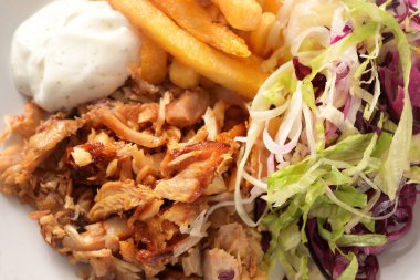 Kızarmış döner kebap tavuk eti, patates kızartması, salata ve tzatziki sosu, yukarıdan yüksek açı, tam kare yakın çekim, seçilmiş odak, dar alan derinliği.
