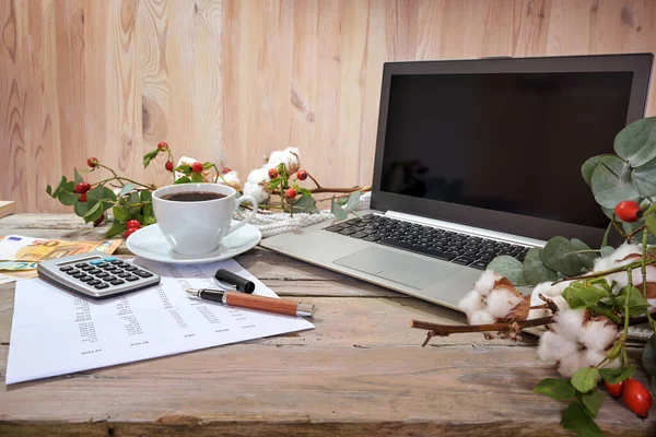 laptop computer, calculator, coffee and money on a rustic table with autumn branches against a wooden background, home office finance accounting, copy space, selected focus, narrow depth of field