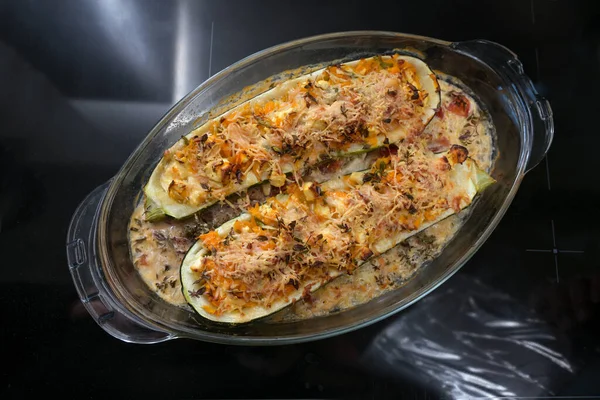 Oven baked zucchini stuffed with vegetables, feta cheese and parmesan in a glass casserole, healthy low carb diet meal, dark background with copy space, high angle view from above, selected focus