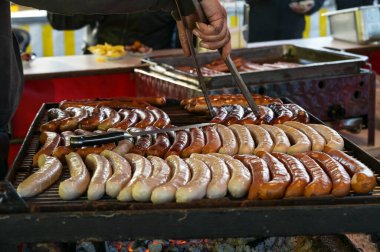 Kirli elli bir adam sokak ızgarasında maşayla sosis çevirir. Alman panayırında ya da Noel pazarında tipik yiyecekler. Seçilmiş odak noktası, dar alan derinliği.