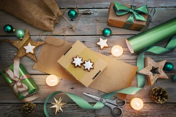 休日の準備 自然の紙と緑のリボンで贈り物を包む ボール 素朴な木製のテーブルの上からのトップビューに灯されたキャンドルのようなクリスマスの装飾 — ストック写真