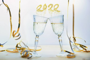 İki şampanya kadehi, yeni yılın şerefine. Baloncuklar 2022 sayısını şekillendiriyor. Açık arkaplan, seçilmiş odak, dar alan derinliği.