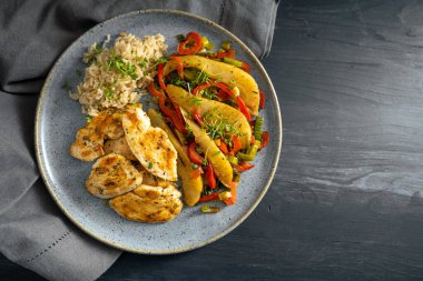 Kızarmış tavuk dilimleri ile tam tahıllı pirinç ve çan biberi sebzeleri, mavi tabakta armut ve pırasa ve koyu gri ahşap masa, kopyalama alanı, yukarıdan üst görünüm, seçilmiş odak noktası