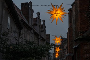 Almanya 'nın eski Lubeck kasabasında tarihi evler arasında dar bir sokakta asılı duran parlak sarı Moravya yıldızları ve Noel, karanlık gökyüzü, kopyalama alanı, seçilmiş odak, çok dar alan derinliği