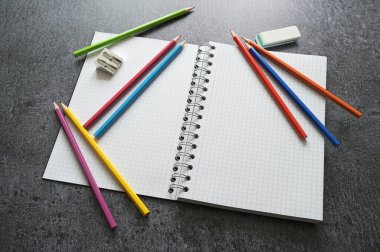 Koyu gri bir tablo üzerinde boş bir spiral defter, pastel kalemler, bileyici ve silgi ile yaratıcı çalışma masası, kopyalama alanı, seçili odak, dar alan derinliği