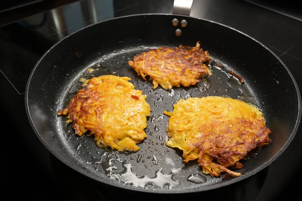 Roasted pancakes from red kuri squash and potato in a black pan, also called pumpkin fritters, rosti or hash browns, vegetable autumn recipe, copy space selected focus, narrow depth of field