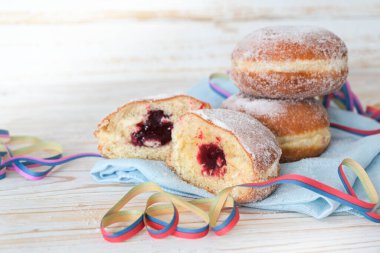 Berlinli çörekler de Krapfen olarak adlandırılır. Parti flamalarıyla dolu bir peçeteye reçel, karnaval ve yeni yıl için tatlı hamur işi, açık ahşap arka plan, kopyalama alanı, seçilmiş odak, çok dar alan derinliği.