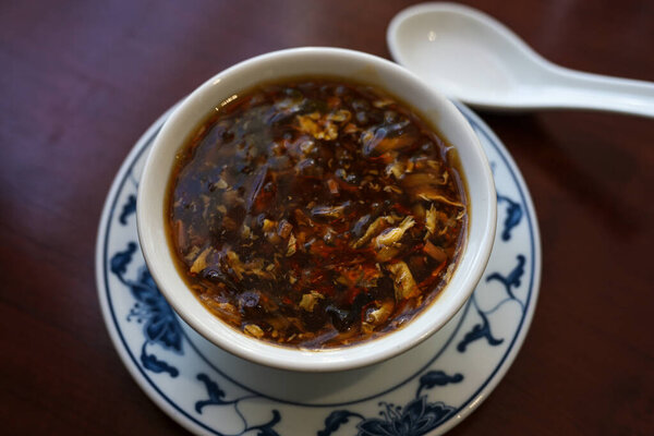 Chinese soup spicy and sour in a bowl with porcelain spoon on a brown table, selected focus, narrow depth of field
