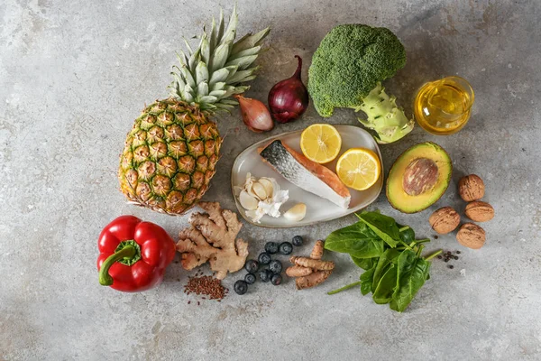 Healthy food with anti-inflammatory and antioxidant effect, set of fresh vegetables, fish, fruits, nuts and spices for a diet concept on light gray stone, copy space, top view from above