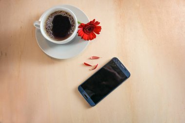Cep telefonu, kahve fincanı ve yaprakları koparılmış kırmızı bir çiçek evet ya da hayır kahin, aşk ve flört çağrısı konsepti, açık ahşap arka plan, kopya alanı, yukarıdan yüksek açılı görüş, seçilmiş odak noktası 
