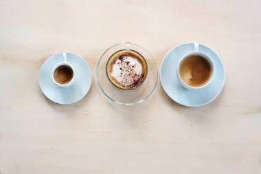 Üç fincan kahve, espresso, cappuccino ve lungo kreması açık ahşap bir masa, fotokopi alanı, yukarıdan yüksek açılı görüş, seçilmiş odaklanma
