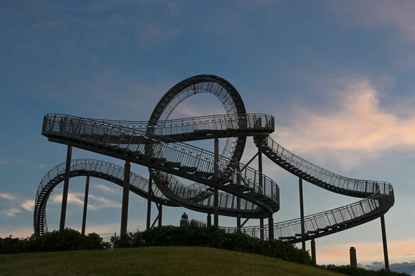 Sihirli Dağ 'da yürüyen Kaplan ve Kaplumbağa roller coaster heykeli. Gül bulutları, sanat kurulumu ve Almanya' nın Angerpark Duisburg şehrinde yer alan koyu mavi gökyüzüne karşı.