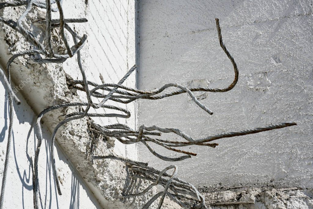 Rebars from iron stick out of a bright concrete wall after demolition, abstract grunge concept for decay or architecture and building themes, copy space, selected focus