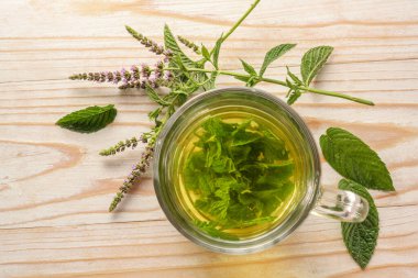 Cam bir fincanda taze nane yaprağından yapılan bitki çayı ve kırsal bir ahşap masa üzerinde çiçek sapları, kopyalama alanı, seçilmiş odak, yukarıdan yüksek açı görünümü