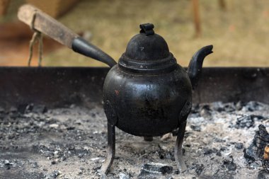 Small iron water kettle on three legs with a wooden handle for boiling coffee or tea on open fire or charcoal embers, copy space, selected focus, narrow depth of field