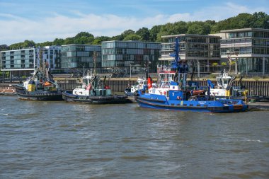 Hamburg, Germany, August 3, 2022: Tugboats in a row in the port of Hamburg in front of modern buildings, they are towing big ships and freighters to the quay, copy space, selected focus