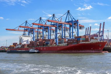 Hamburg, Germany, August 3, 2022: Large container cargo ship is unloaded at the terminal with cranes in the port of Hamburg, concept of transport, shipping and delivery, blue sky, copy space, selected focus