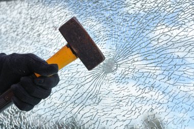 hand of a man is hitting a window from safety glass with a heavy hammer, vandalism and burglary concept, copy space, selected focus