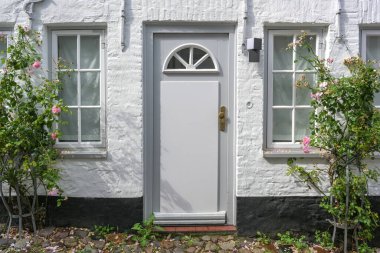 Front door in a white painted facade of a small historic brick house with roses on the facade in the old town of Flensburg, Germany, selected focus
