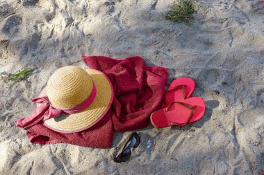 Summer beach vacations, straw hat and flip flops on a red towel in the sand near the tourist resort Boltenhagen, Baltic Sea, Germany, copy space, view from above, selected focus
