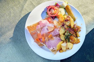 Sauerfleisch mit Bratkartoffeln or sour pickled meat in aspic with fried potatoes, traditional German and Austrian dish on a white plate and a rustic table, copy space, view from above, selected focus