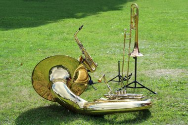 Various musical brass instruments like sousaphone, trombone and saxophone placed on the lawn in the park and waiting to be used in the music band, copy space clipart