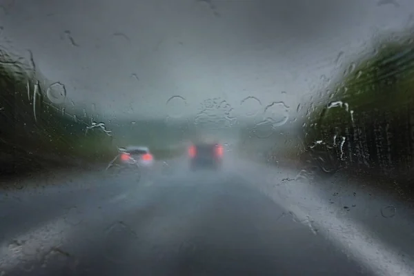 Heavy rain on the highway, thick drops on the windshield and blurred cars with red taillights on the dark road, dangerous weather while driving, traffic and transport concept, copy space, selected focus