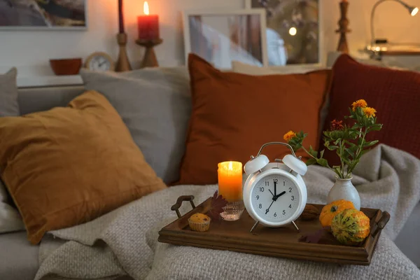 夏時間を節約した後の秋に戻って時間を示す白いヴィンテージ目覚まし時計 キャンドルと暖かい色の秋の装飾と木製のトレイ居心地の良いソファ コピースペース 選択されたフォーカス — ストック写真