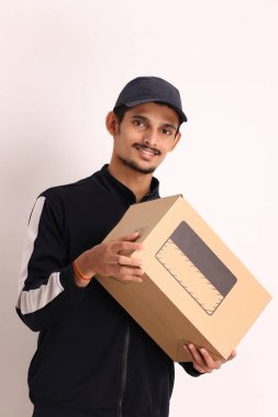 Kahverengi kutulu, siyah tişörtlü, beyaz arka planda yüz ifadeleri olan, traşsız Hintli kurye çocuk. 