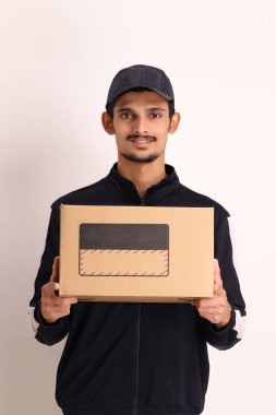 Kahverengi kutulu, siyah tişörtlü, beyaz arka planda yüz ifadeleri olan, traşsız Hintli kurye çocuk. 