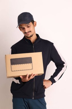 Kahverengi kutulu, siyah tişörtlü, beyaz arka planda yüz ifadeleri olan, traşsız Hintli kurye çocuk. 