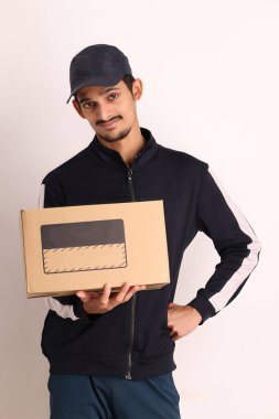 Kahverengi kutulu, siyah tişörtlü, beyaz arka planda yüz ifadeleri olan, traşsız Hintli kurye çocuk. 