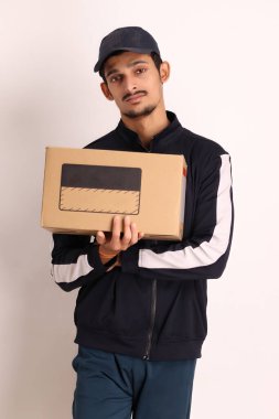 Kahverengi kutulu, siyah tişörtlü, beyaz arka planda yüz ifadeleri olan, traşsız Hintli kurye çocuk. 