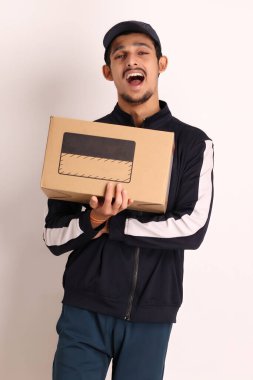 Kahverengi kutulu, siyah tişörtlü, beyaz arka planda yüz ifadeleri olan, traşsız Hintli kurye çocuk. 