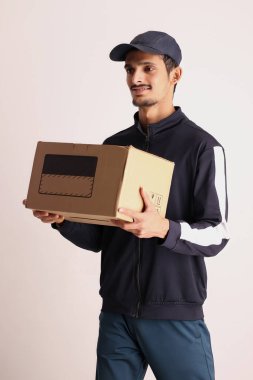 Kahverengi kutulu, siyah tişörtlü, beyaz arka planda yüz ifadeleri olan, traşsız Hintli kurye çocuk. 