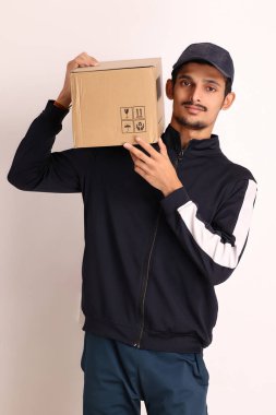 Kahverengi kutulu, siyah tişörtlü, beyaz arka planda yüz ifadeleri olan, traşsız Hintli kurye çocuk. 