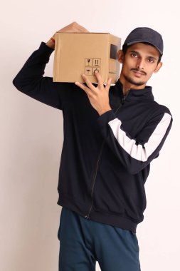 Kahverengi kutulu, siyah tişörtlü, beyaz arka planda yüz ifadeleri olan, traşsız Hintli kurye çocuk. 