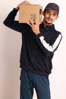 Kahverengi kutulu, siyah tişörtlü, beyaz arka planda yüz ifadeleri olan, traşsız Hintli kurye çocuk. 