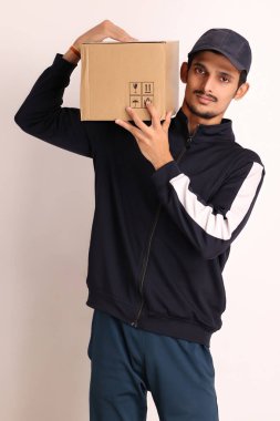Kahverengi kutulu, siyah tişörtlü, beyaz arka planda yüz ifadeleri olan, traşsız Hintli kurye çocuk. 