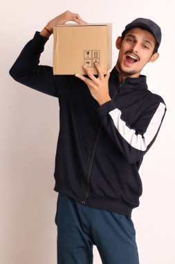 Kahverengi kutulu, siyah tişörtlü, beyaz arka planda yüz ifadeleri olan, traşsız Hintli kurye çocuk. 