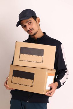 Kahverengi kutulu, siyah tişörtlü, beyaz arka planda yüz ifadeleri olan, traşsız Hintli kurye çocuk. 