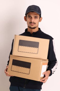 Kahverengi kutulu, siyah tişörtlü, beyaz arka planda yüz ifadeleri olan, traşsız Hintli kurye çocuk. 